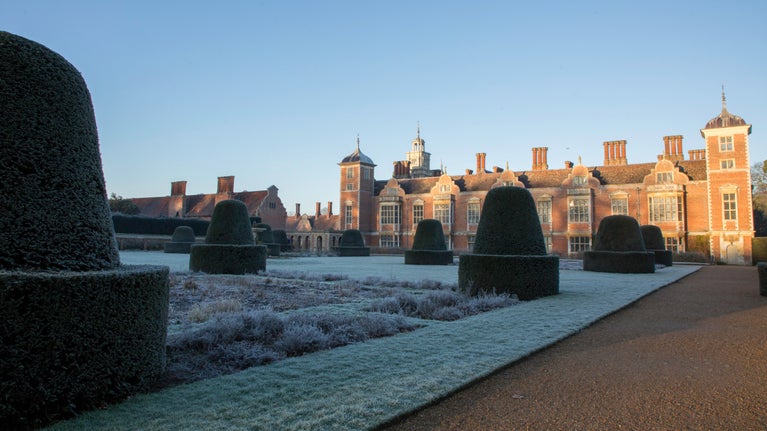 A frosty parterre garden, with grass and clipped shaped hedges, with a large period house in the background at Blickling, Norfolk
